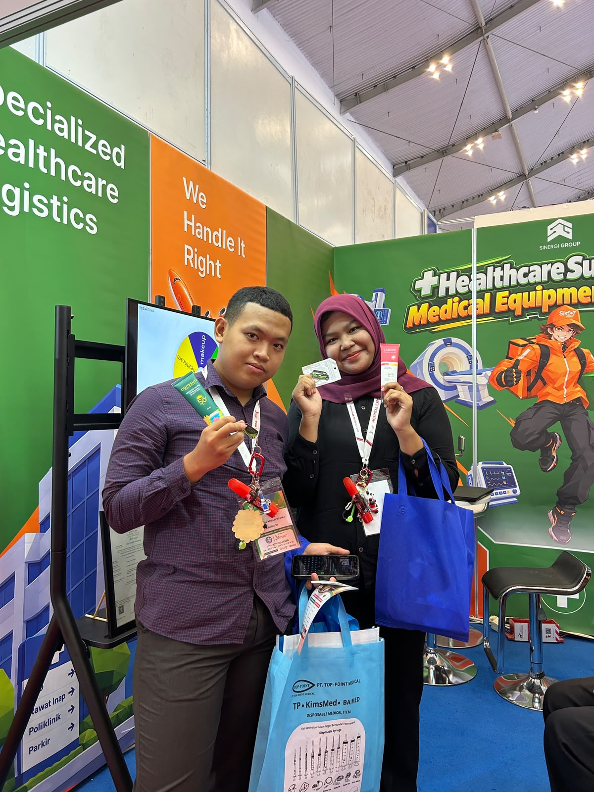 Pengunjung memegang hadiah di booth S-LOG dengan layar permainan spin wheel pada HOSPEX 2026